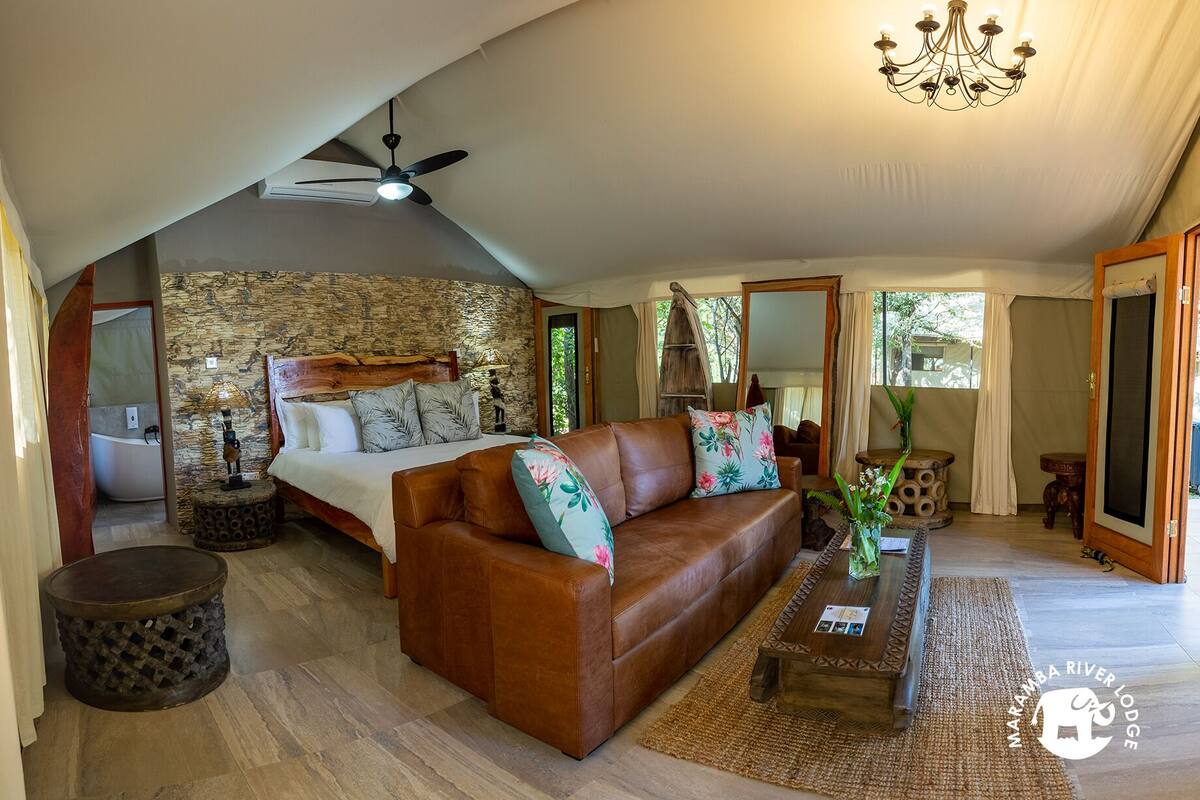 A spacious room with a stone wall, a bed, a brown leather sofa, a wooden coffee table, and a chandelier.