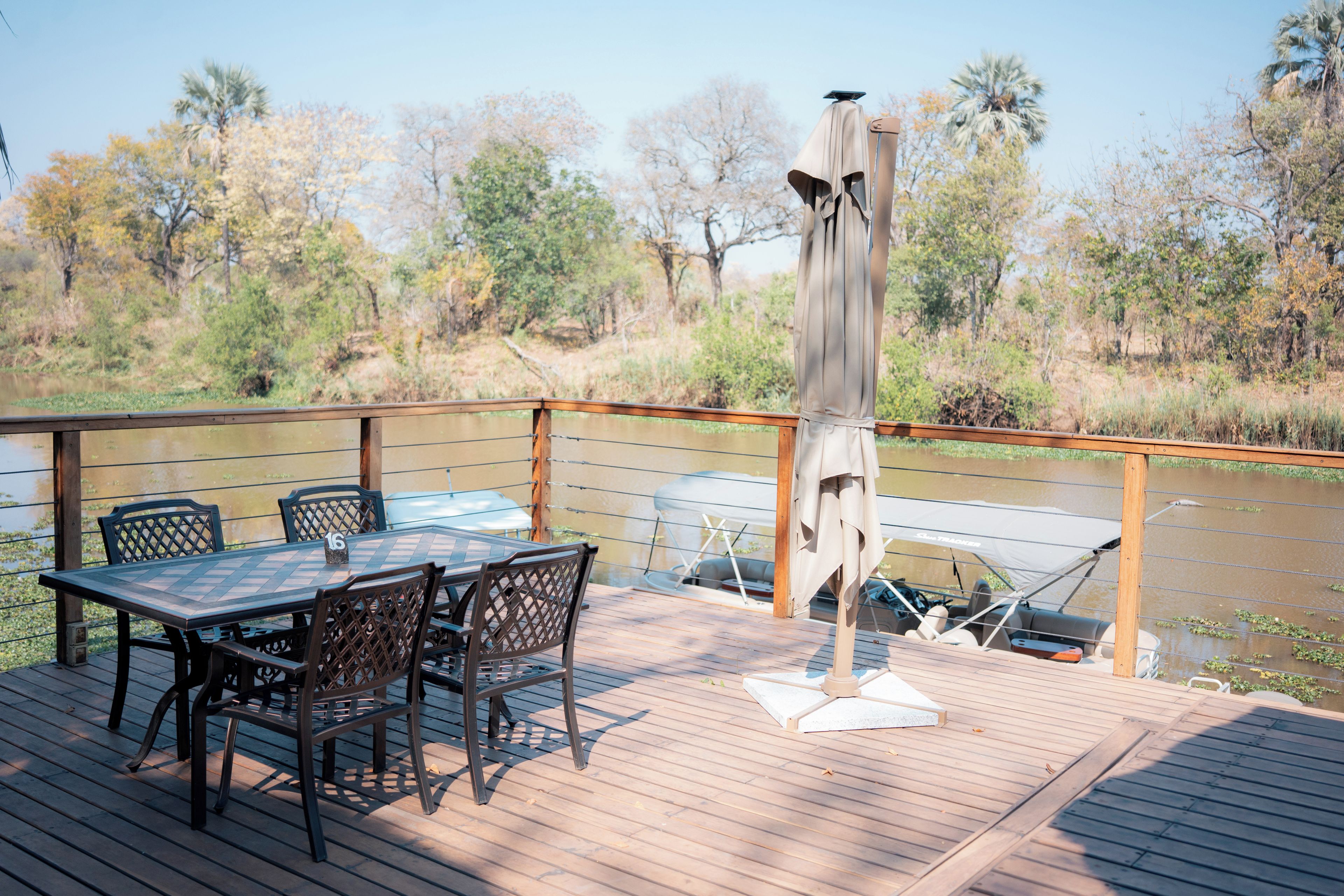 A deck with a table and chairs, overlooking a body of water with trees in the background.