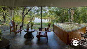 A covered outdoor seating area with a hot tub, wooden chairs, and a table with a candle. - Maramba River Lodge (Livingstone)