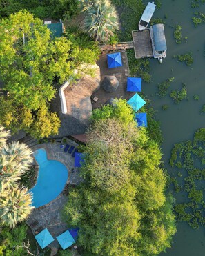 An aerial view of a resort with a swimming pool, lounge chairs, and a dock extending into a body of water. - Maramba River Lodge (Livingstone)