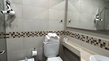 Un baño moderno con inodoro, bidé y lavamanos, paredes con azulejos y un espejo.