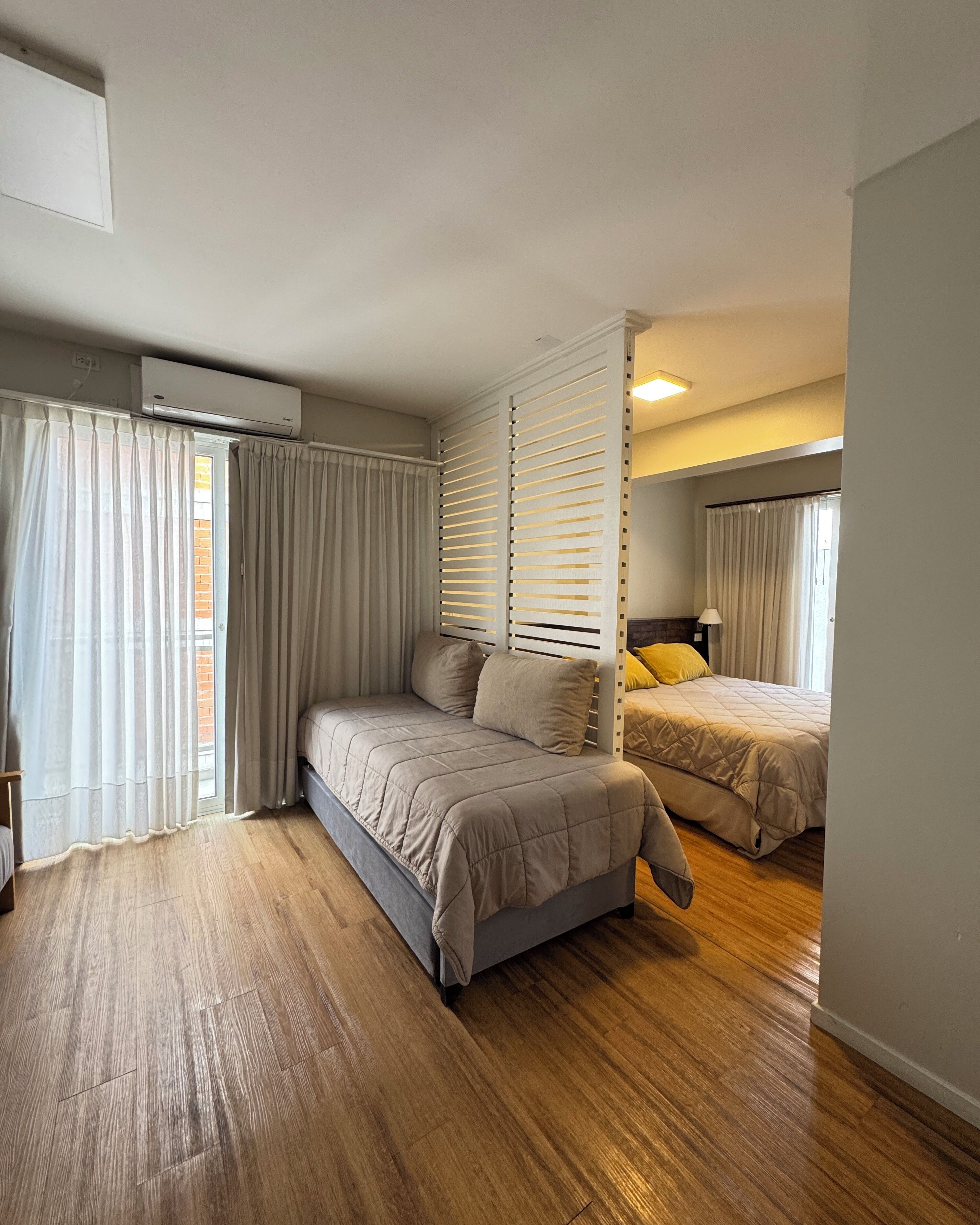 Un dormitorio con cama, mesita de noche y ventana con cortinas.