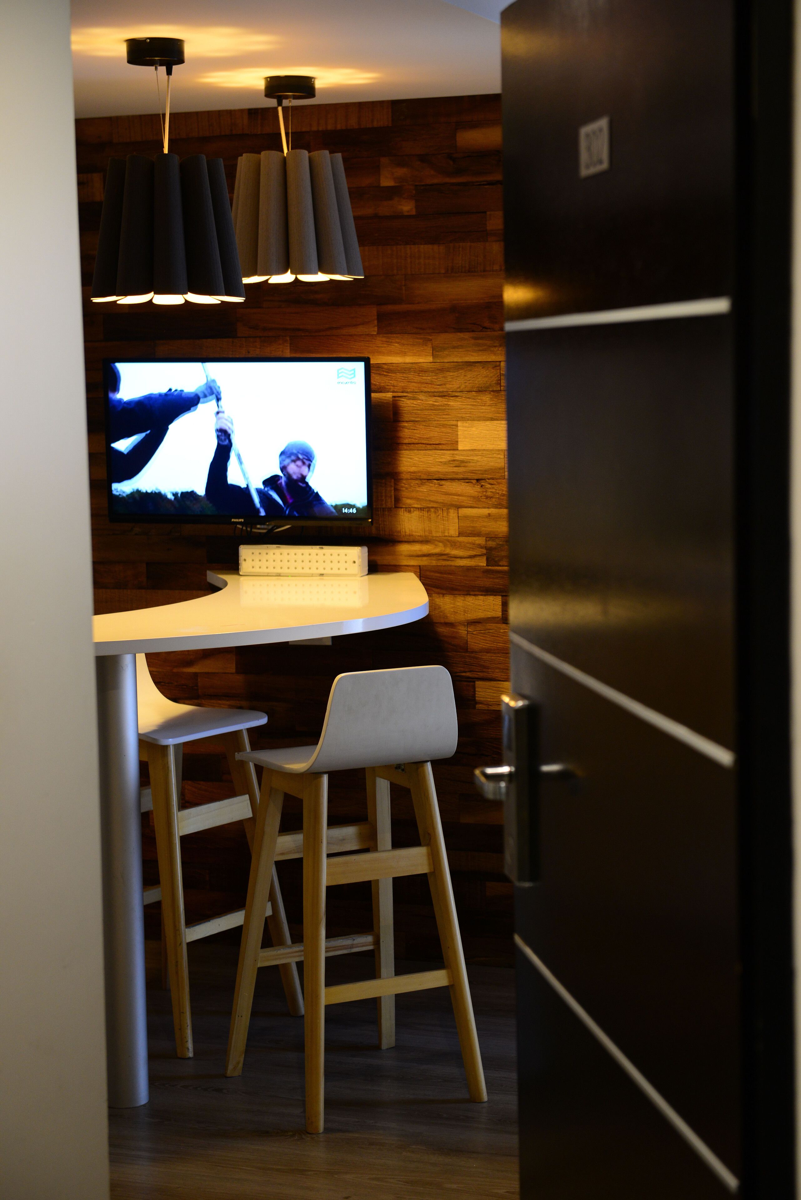 A modern kitchen with a built-in refrigerator, a wooden accent wall, a bar area with a white countertop, and pendant lighting.