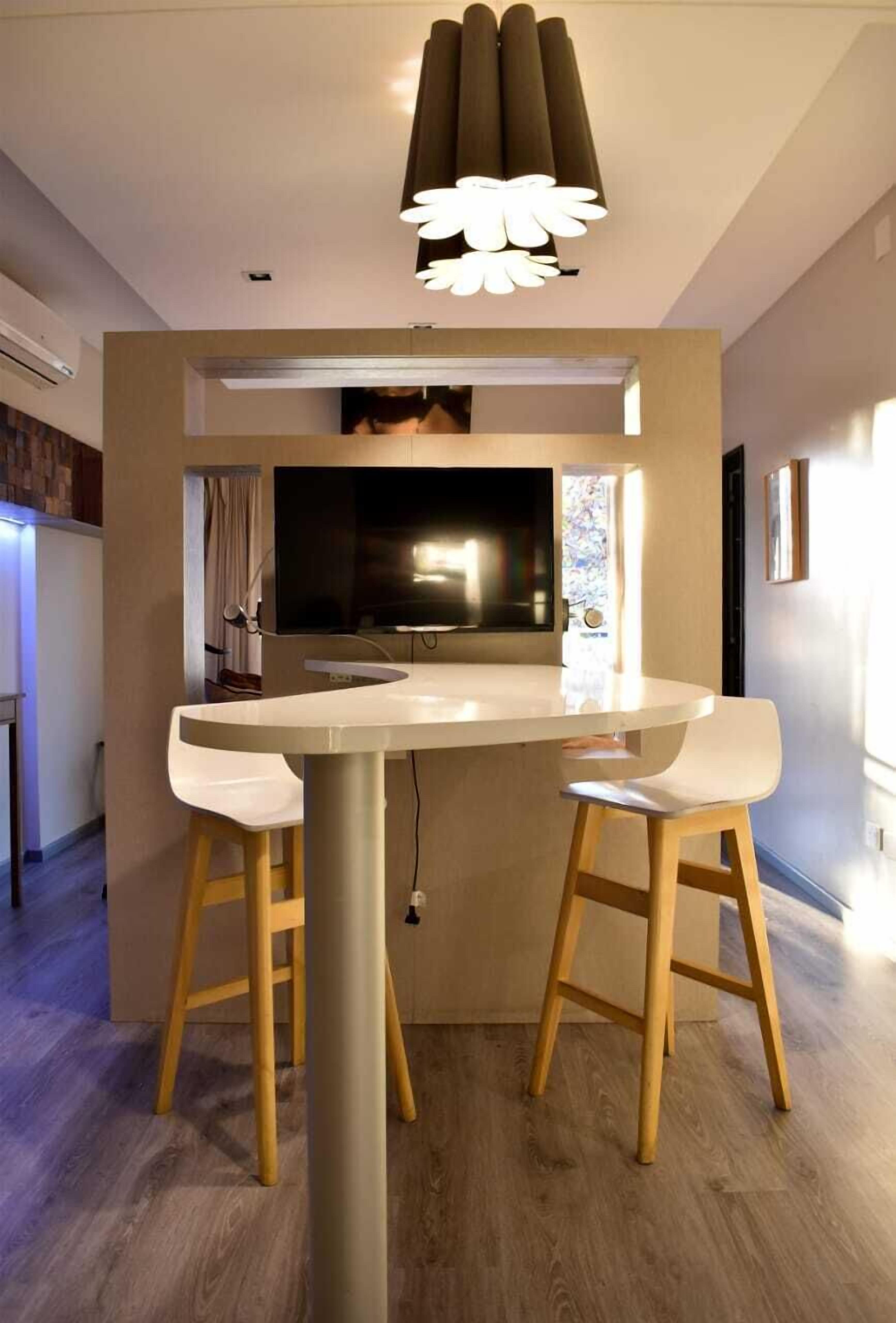 A modern kitchen with a central island, two white bar stools, and a unique ceiling light fixture.
