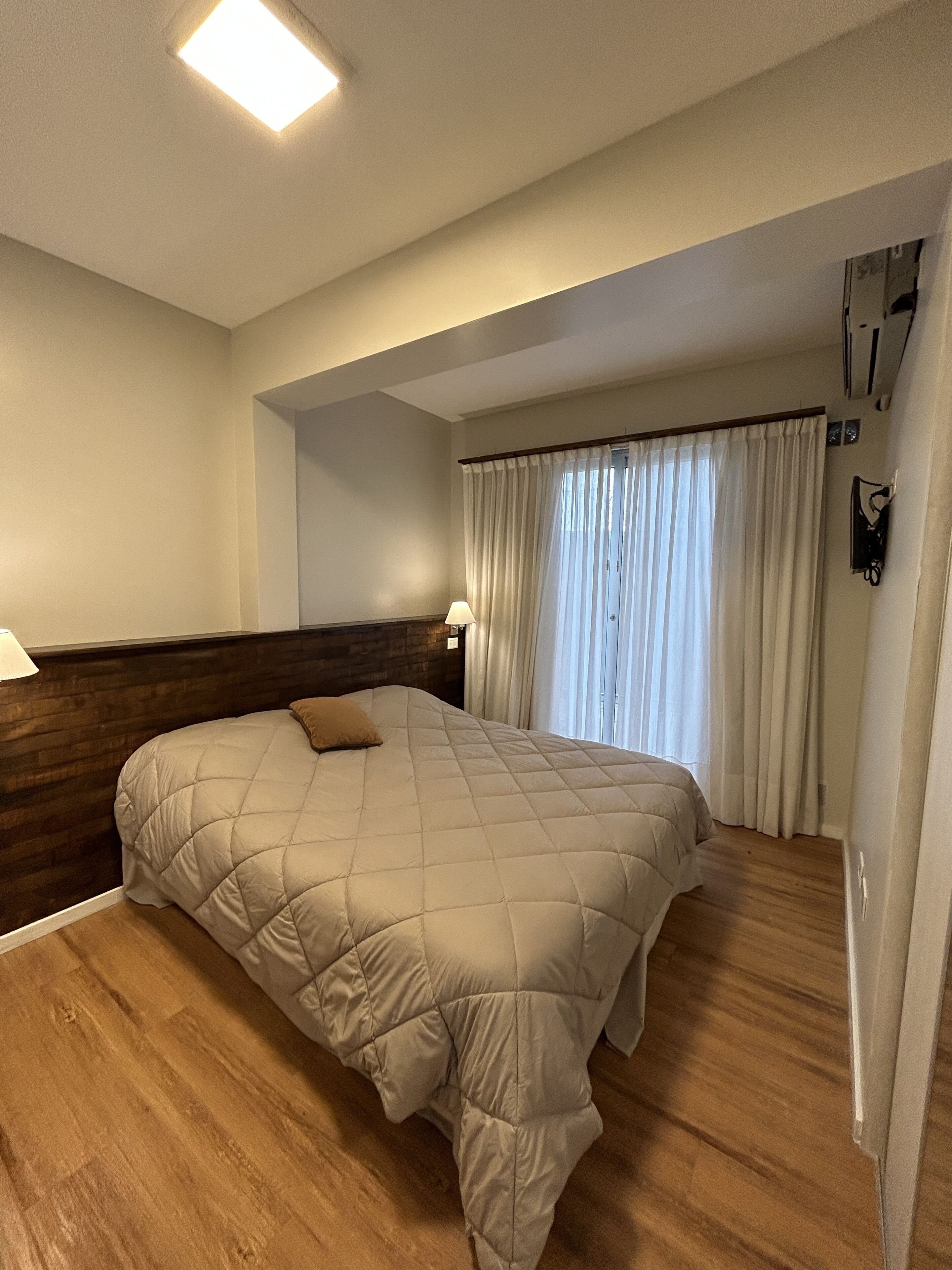 A hotel room with a large bed, wooden headboard, and a window with curtains.