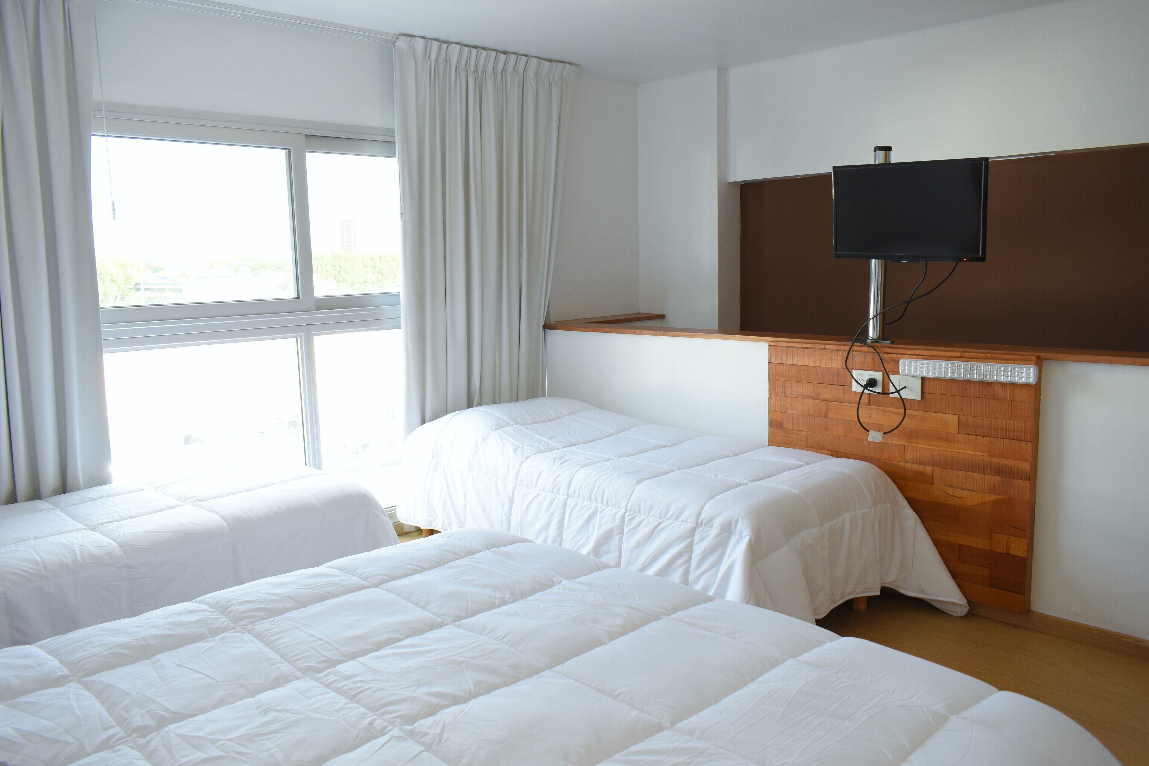 Habitación de hotel con dos camas, un televisor instalado en un panel de madera y una ventana con cortinas.