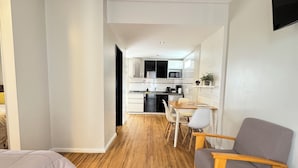 A modern hotel room with a wooden floor, a bed, a seating area with a sofa and chairs, and a kitchenette in the background. - Syrah Suites (Buenos Aires)