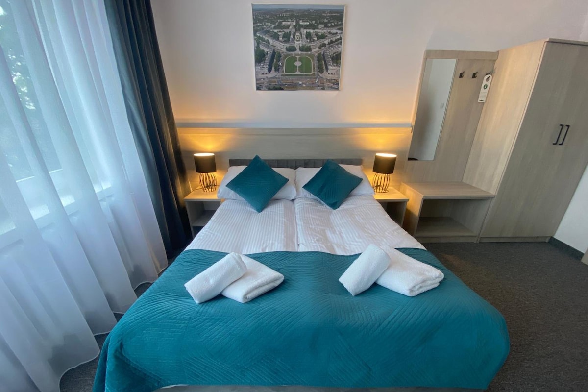 Habitación de hotel con una cama grande, dos mesitas de noche con lámparas, un armario y vistas a la ciudad.