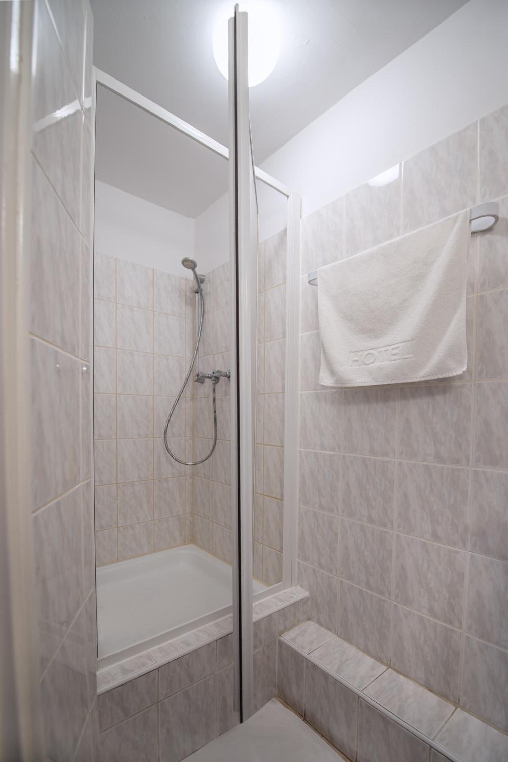 A shower with a glass door, a handheld showerhead, and a towel rack with a towel.