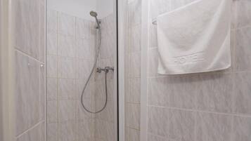 A shower with a glass door, a handheld showerhead, and a towel rack with a towel.