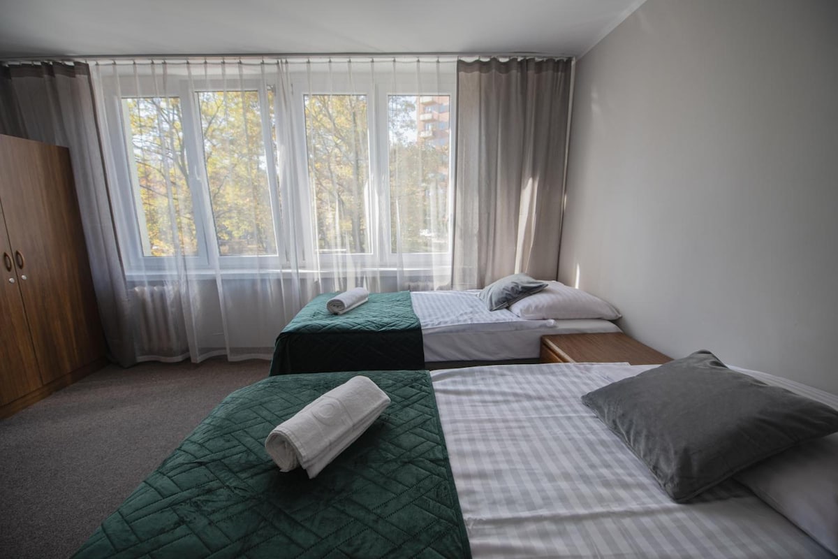 A bedroom with two beds, a wardrobe, and a window with curtains.