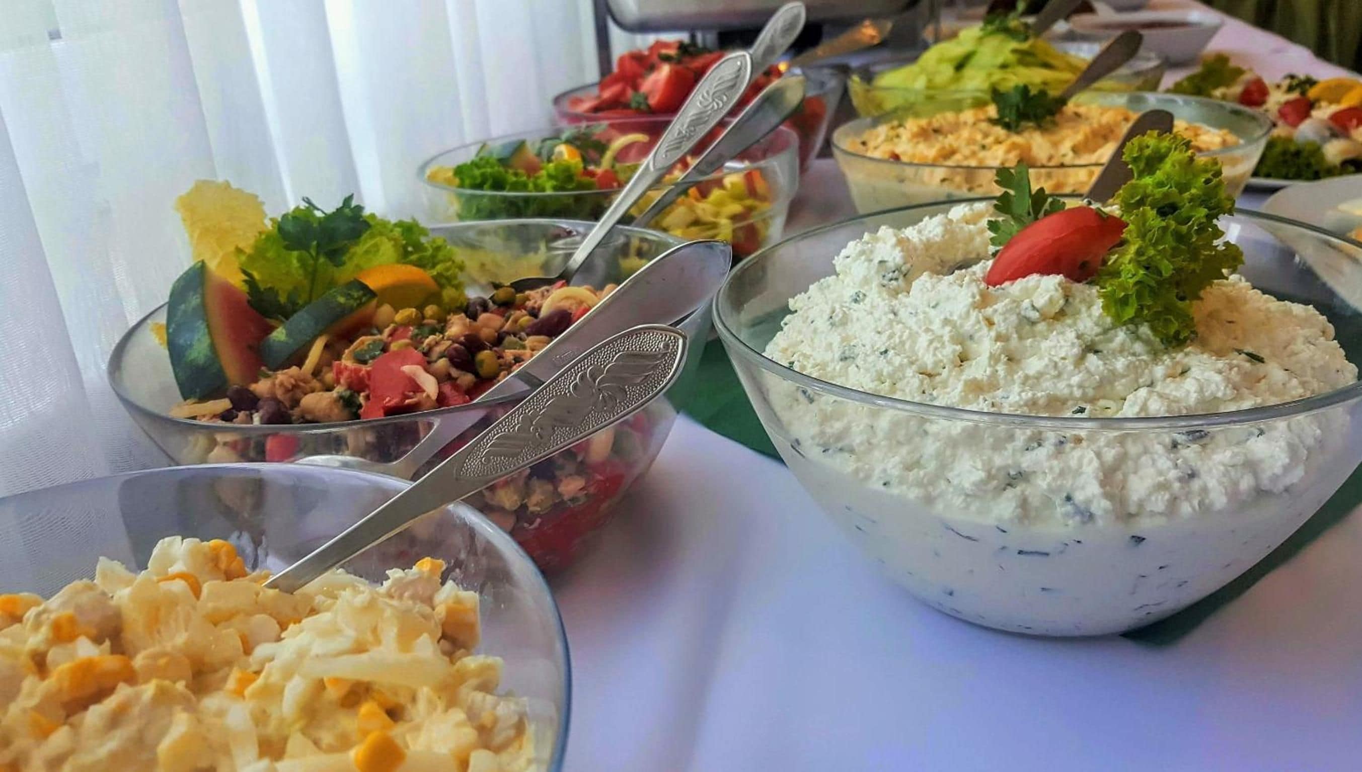 A table with various food items in clear bowls, including a bowl of salad with a tomato garnish.