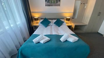 A hotel room with a large bed, two bedside tables with lamps, a wardrobe, and a cityscape view.