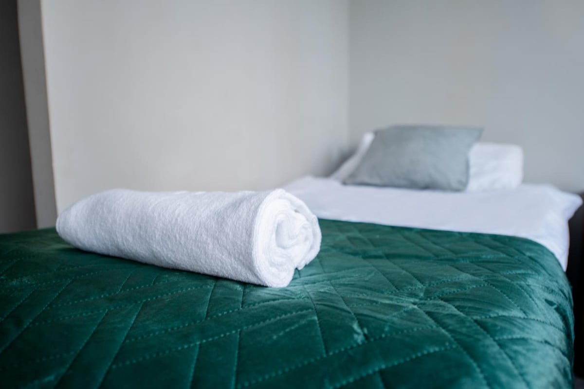 Una cama bien hecha con una colcha verde y una toalla blanca enrollada encima.