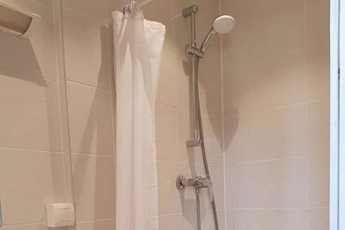 A small, enclosed shower area with a white shower curtain, a handheld showerhead, and a wall-mounted faucet.
