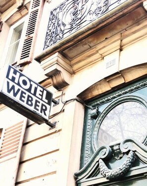 A hotel sign labeled "HOTEL WEBER" mounted on a building with ornate architectural details and a large, decorative window. - budget hotel weber-Strasbourg Centre Gare (Strasbourg)