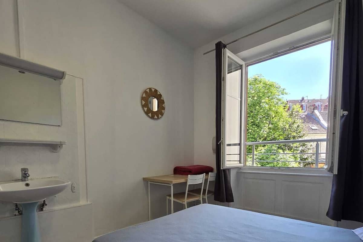A bedroom with a bed, a desk, a chair, a window, and a sink.
