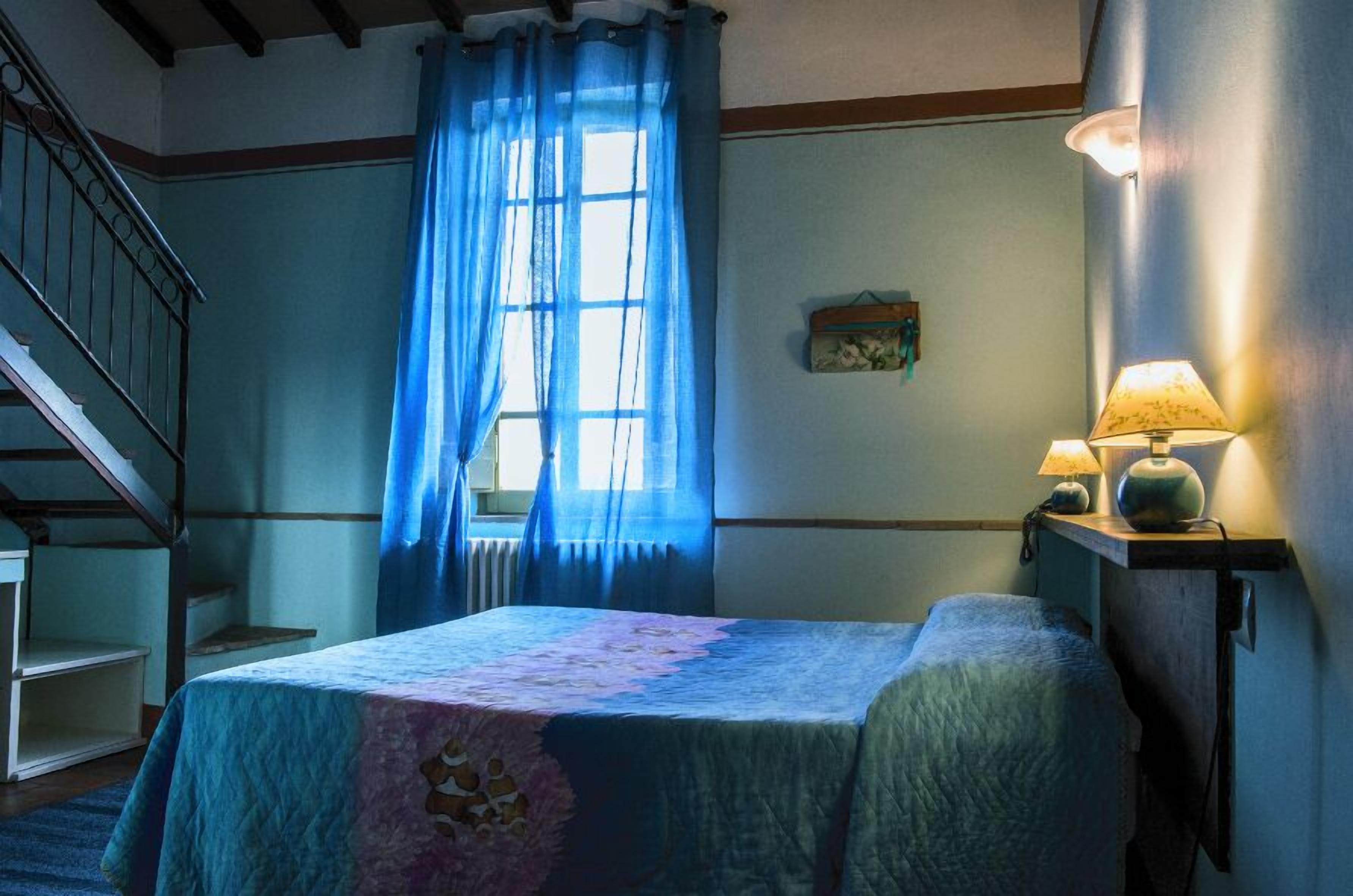 Ein Schlafzimmer mit einem Bett, einem Nachttisch mit Lampen, einem Fenster mit blauen Vorhängen und einer Treppe.