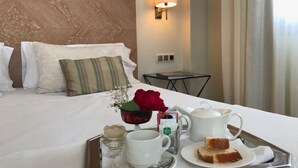 A neatly made bed with pillows, a bedside table with a lamp, and a tray with breakfast items including a cup, a teapot, and a slice of cake. - Hotel Entredos (Guijuelo)