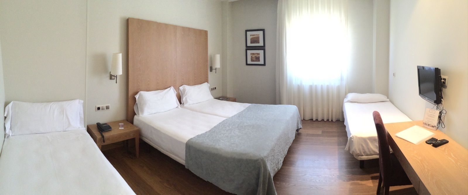 Une chambre d’hôtel avec deux lits simples, un grand lit, un bureau avec une chaise, une télévision et une fenêtre avec des rideaux.