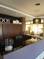 Un moderno vestíbulo de hotel con una recepción, una zona de estar con una silla azul y una lámpara decorativa grande.