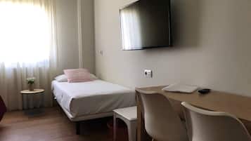 Habitación de hotel con cama, escritorio, silla, televisor y una mesita con una planta.