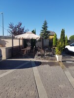 Un patio al aire libre con mesas y sillas, un área de estar cubierta y macetas con plantas.