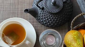 Une table dressée avec une tasse de thé, une part de gâteau, une théière, une bougie et un panier de fruits.