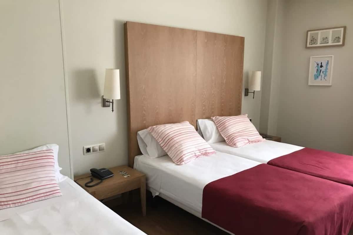 Ein Hotelzimmer mit zwei Betten, einem Holz-Kopfteil, Nachttischlampen und Bildern an der Wand.