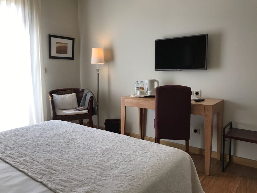 A hotel room with a bed, a desk, a chair, a television, and a lamp.