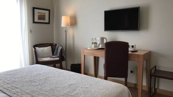 A hotel room with a bed, a desk, a chair, a television, and a lamp.