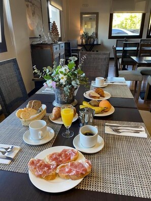 Una mesa de desayuno servida con cruasanes, pan, fruta, café y jugo.
