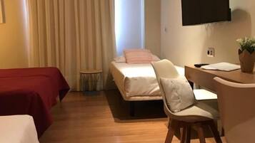 Ein Hotelzimmer mit zwei Betten, einem Schreibtisch, einem Sessel, einem Fernseher und einem Fenster mit Vorhängen.