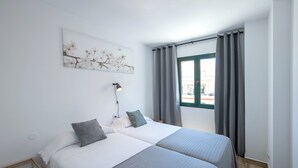 A double room with two beds, a bedside table, a lamp, a window with curtains, and a wall-mounted artwork. - Los Rosales (Brena Baja)