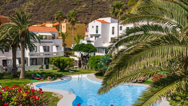 A pool surrounded by palm trees and a white building with a red roof. - Los Rosales (Brena Baja)