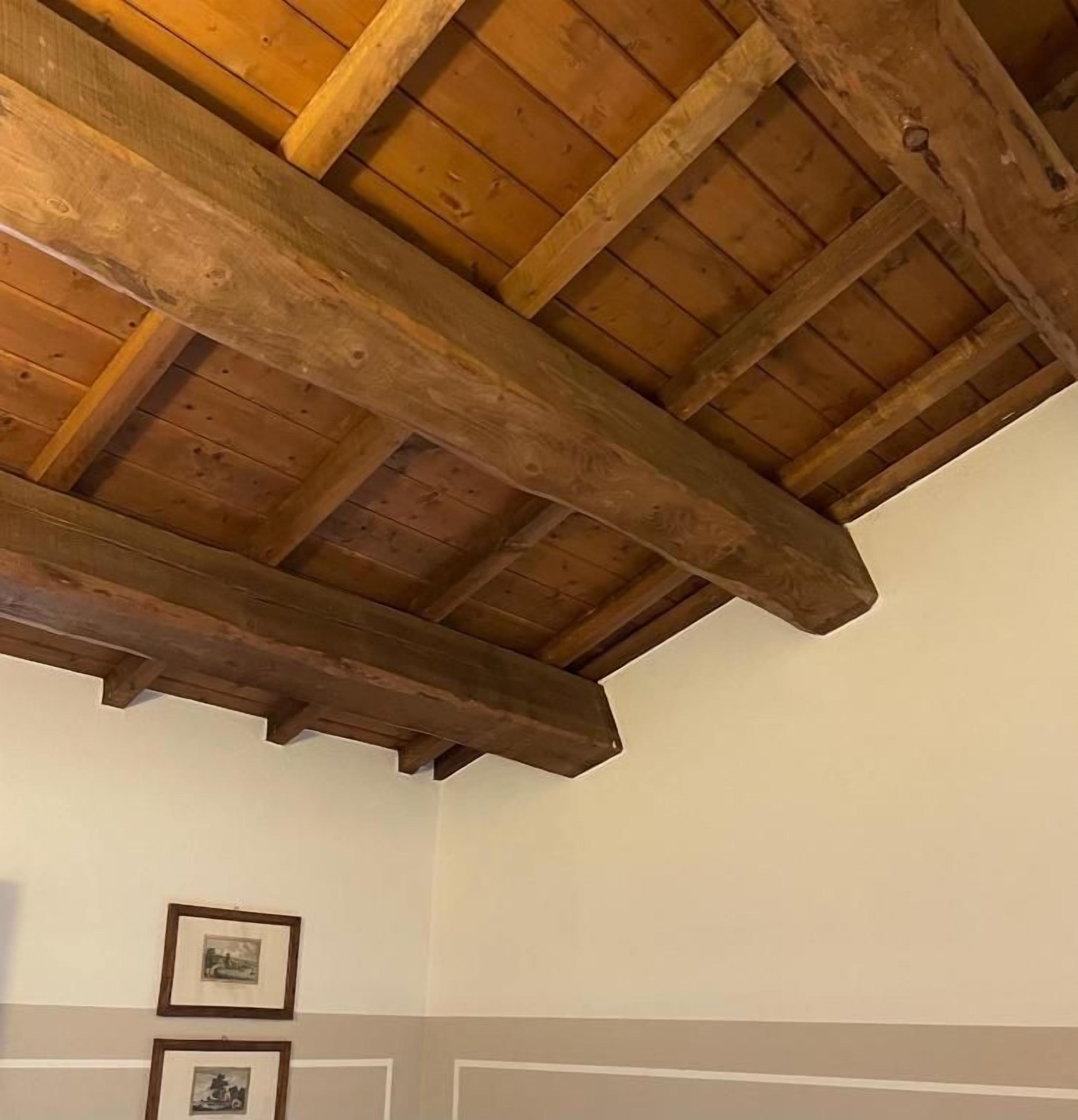 Quarto com vigas de madeira no teto, paredes brancas e duas imagens emolduradas.