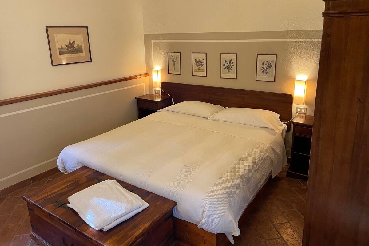 A neatly made bed with a white comforter and pillows, flanked by two bedside tables with lamps, in a room with a wooden headboard and a framed picture on the wall.