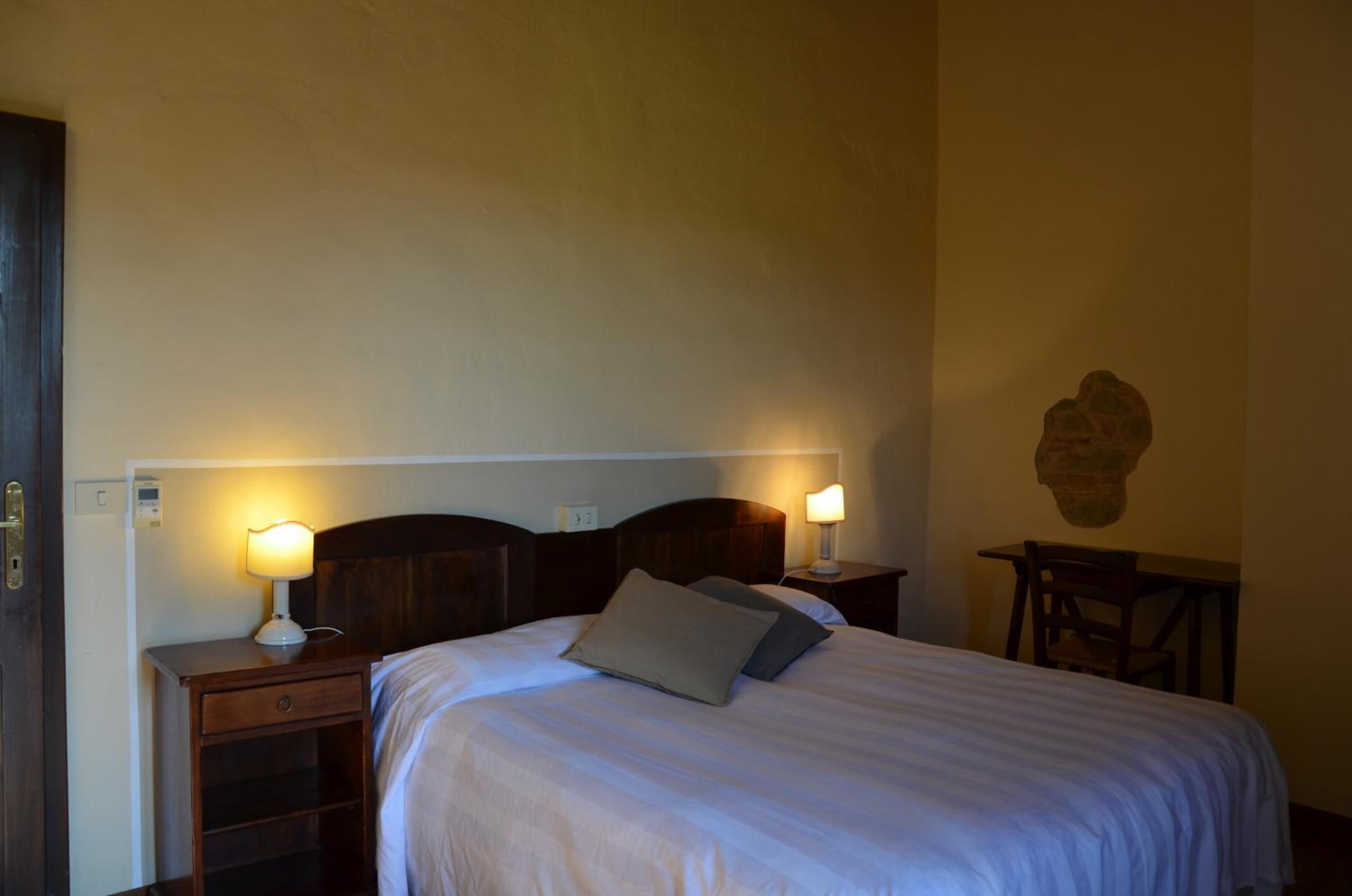A neatly made bed with two bedside lamps, a wooden nightstand, and a small table with a chair.