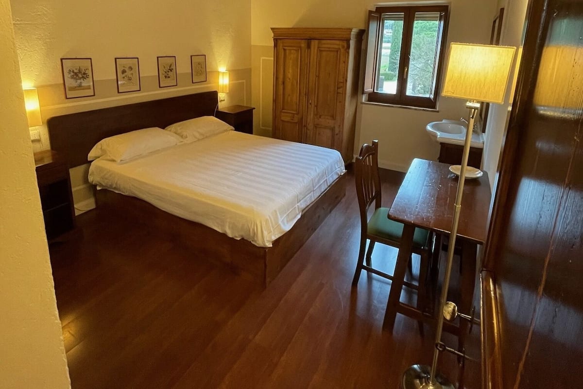 A bedroom with a wooden ceiling, a bed, a desk with a chair, and a window.