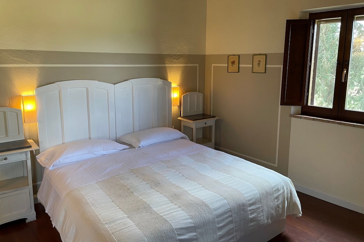 A neatly made bed with a striped bedspread, a bedside table with a lamp, and a window with curtains.