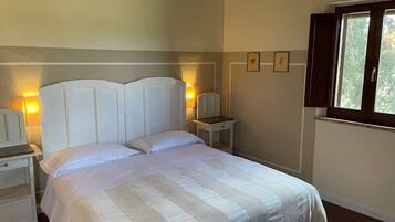 Una cama bien hecha con colcha a rayas, una mesita de noche con lámpara y una ventana con cortinas.