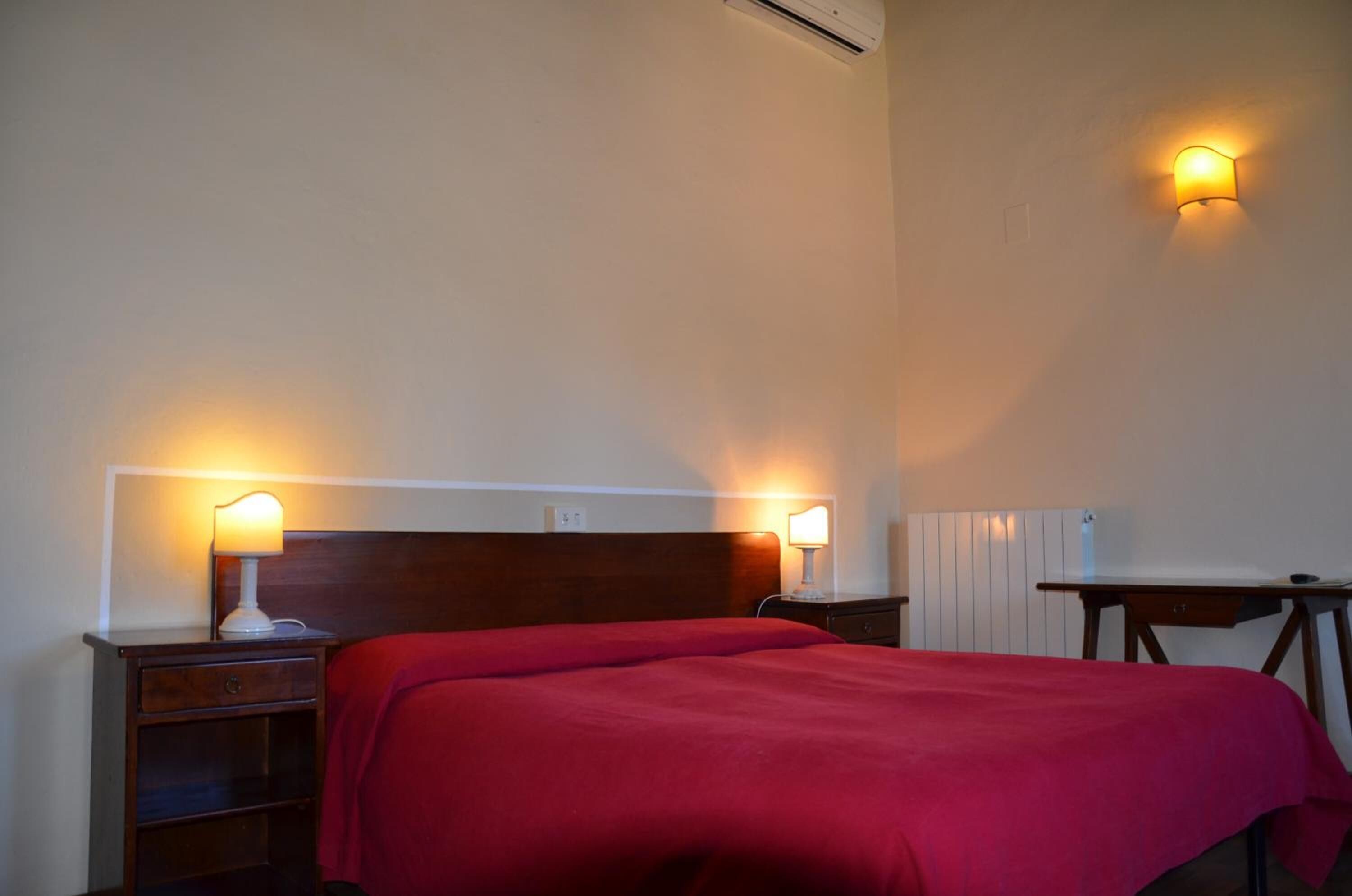 A hotel room with a bed, two bedside tables with lamps, a small desk, and a wall-mounted light fixture.