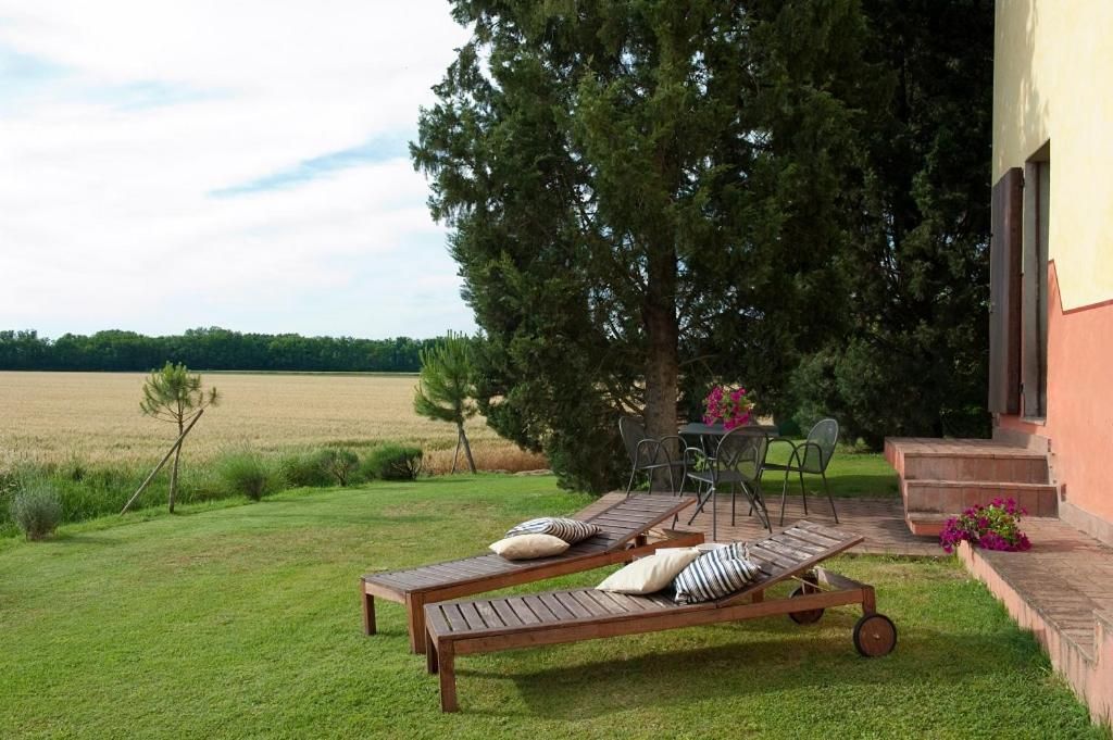 Eine Terrasse mit zwei Holzliegen, einem Tisch und Stühlen sowie Blick auf ein Feld.