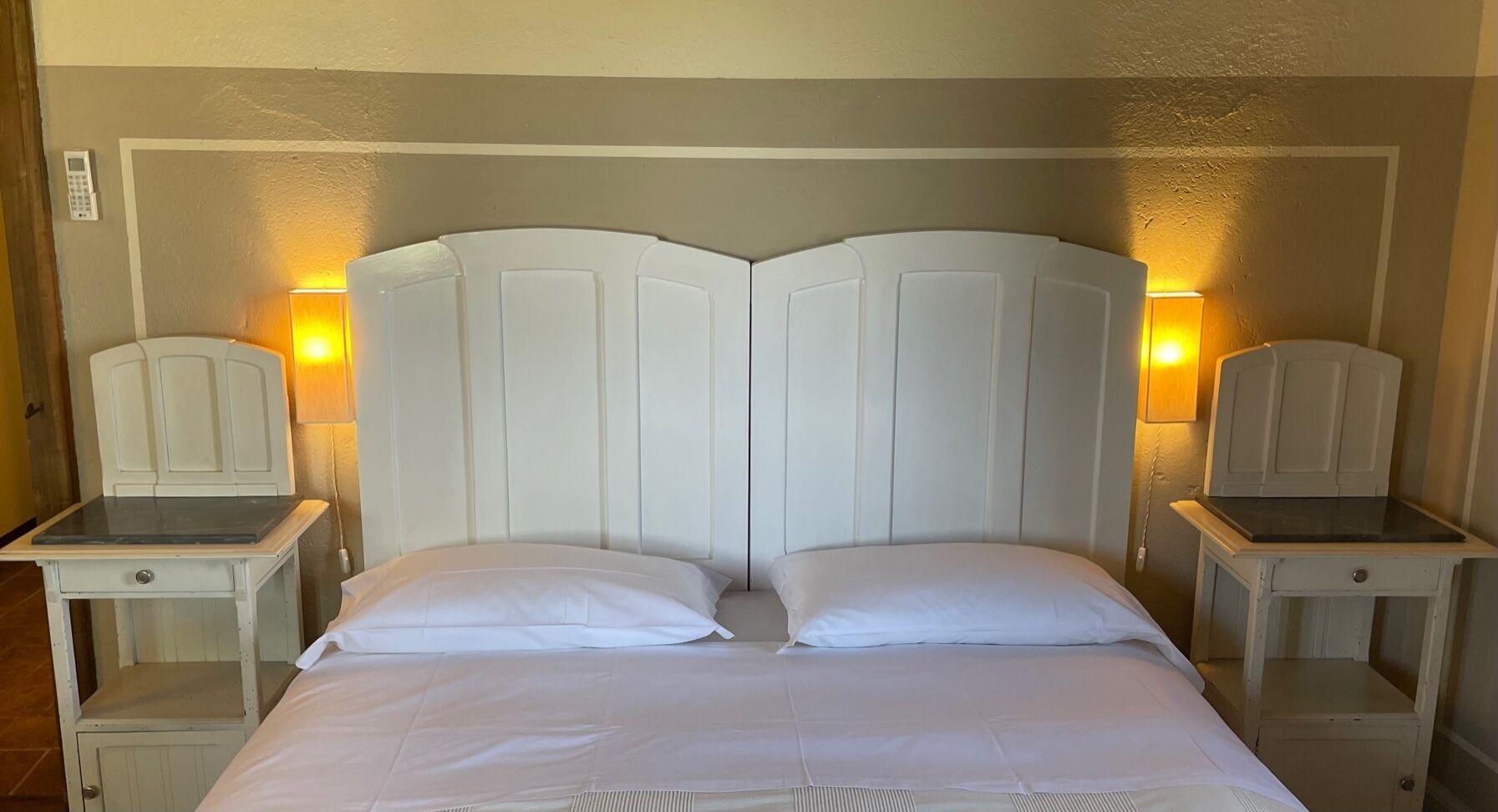 A double bed with a white headboard and two bedside tables, each with a lamp.