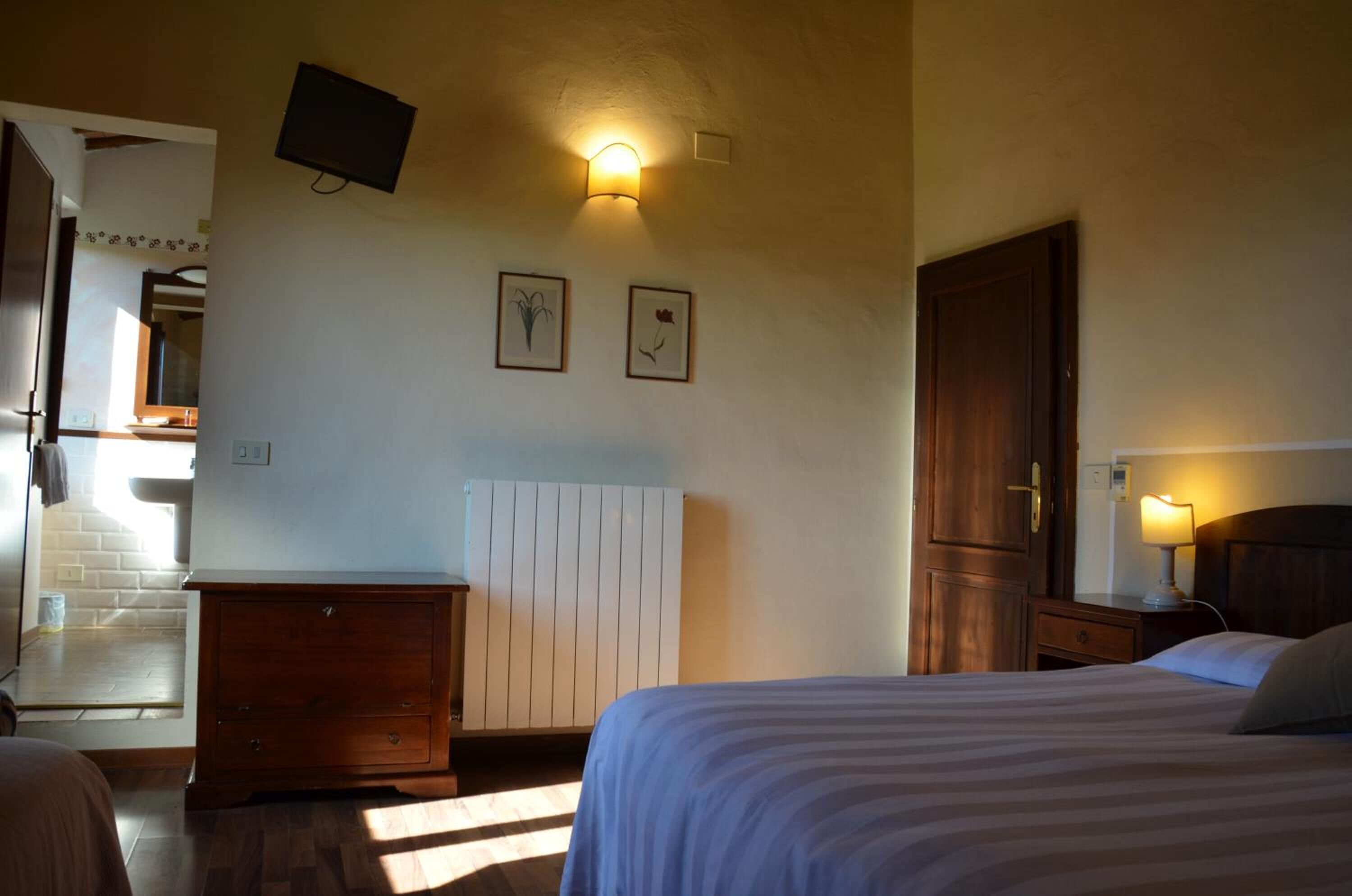 A bedroom with a bed, a dresser, a nightstand, a wall-mounted TV, and a radiator.