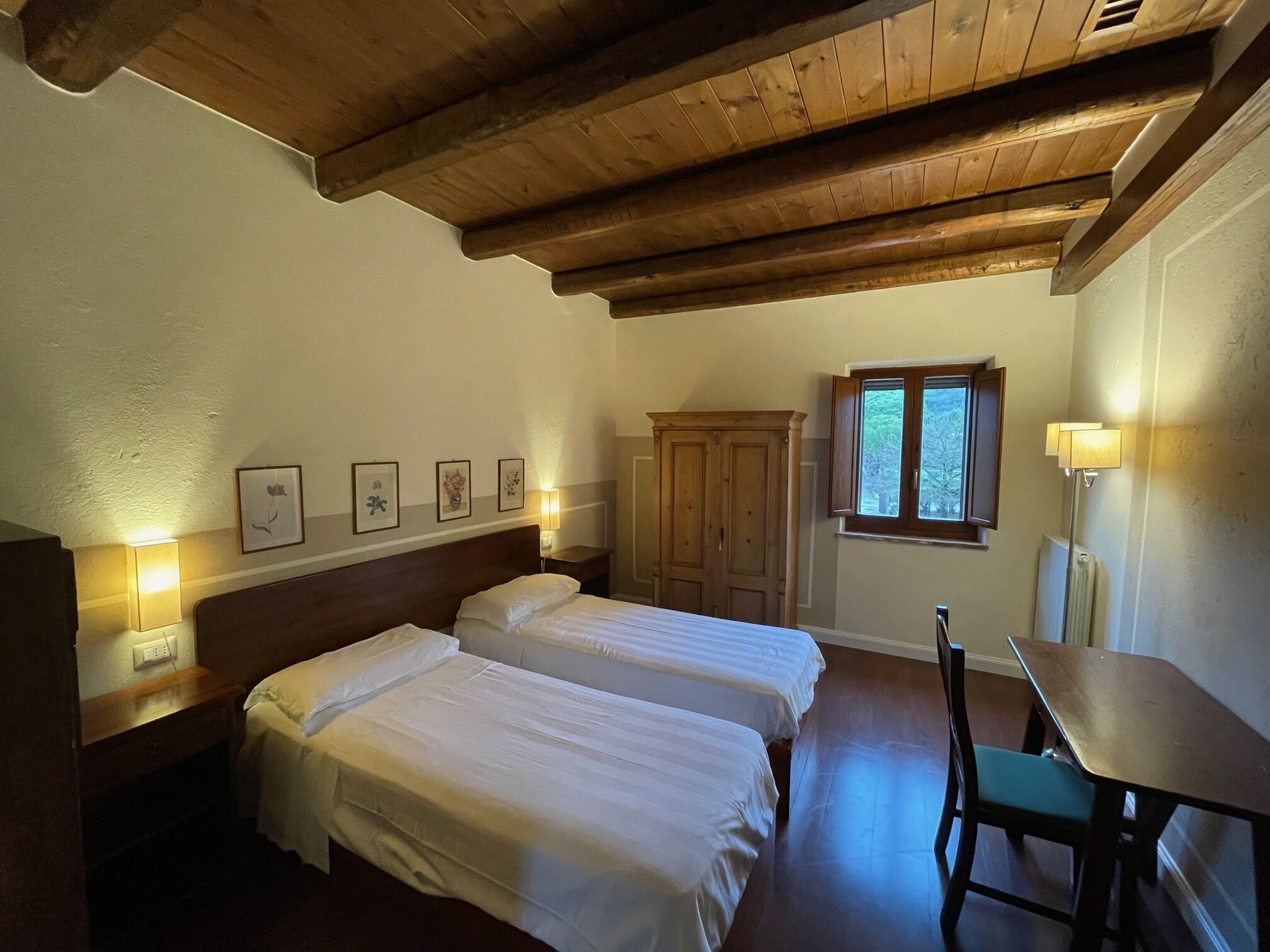 Une chambre avec deux lits, une armoire en bois, une fenêtre et une table avec une chaise.