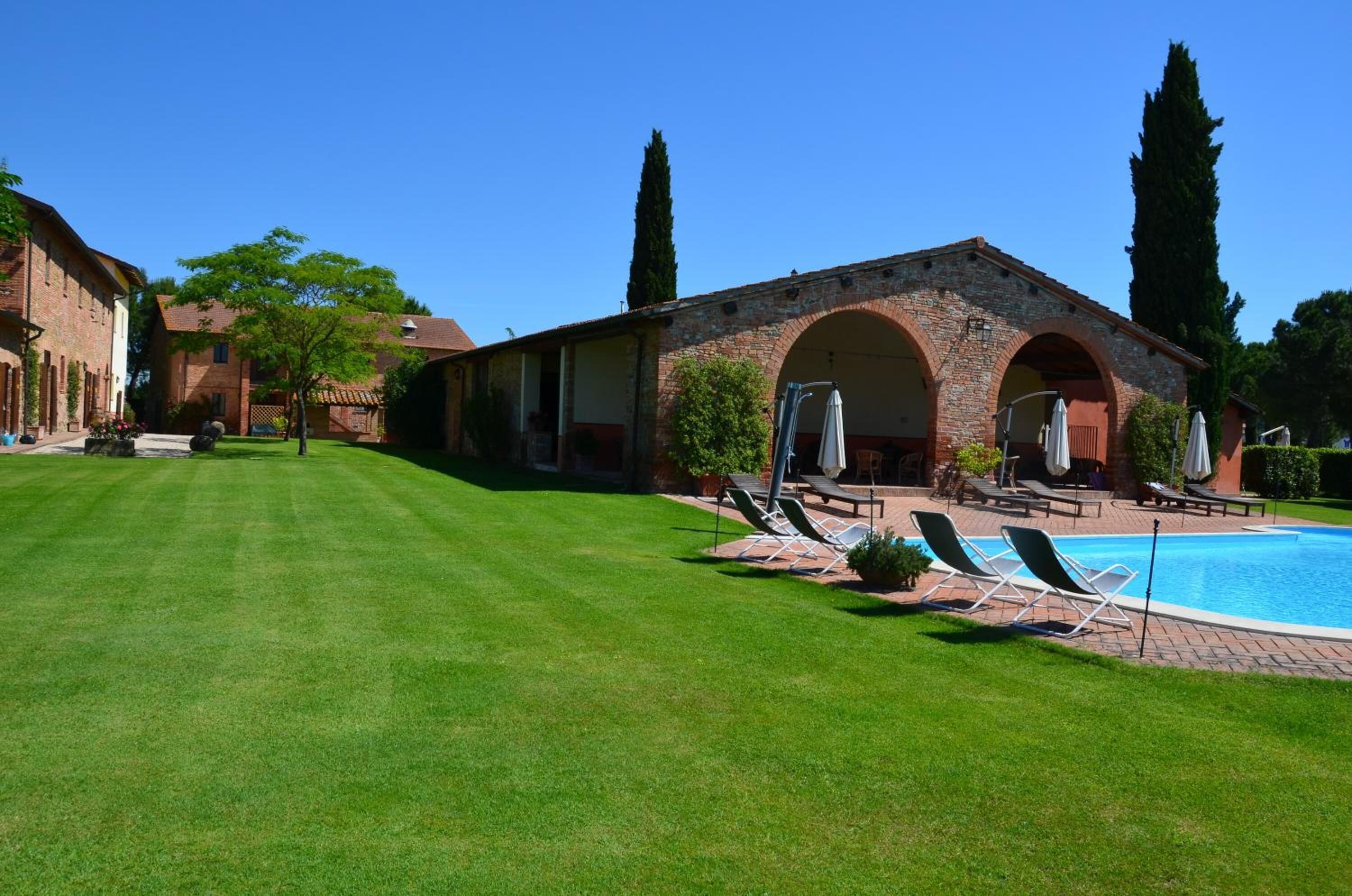 Zona de piscina amb gandules, edifici de maó amb arcades i gespa ben cuidada.