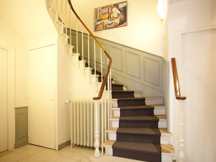 A staircase with white railings and a wooden handrail, leading to a landing with a radiator and a door.
