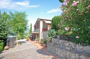 A stone building with a tiled roof, surrounded by lush greenery and flowering plants.
