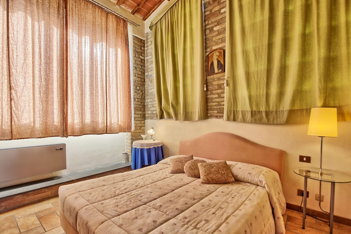 A hotel room with a bed, a side table with a lamp, a TV, and curtains.
